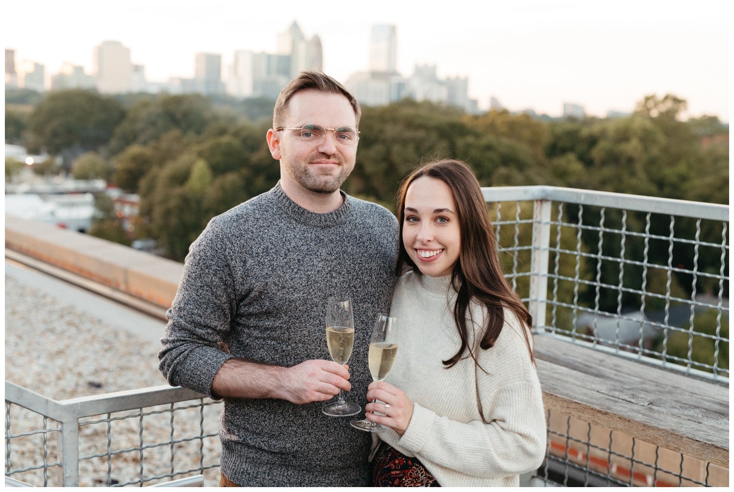 Engaged couple toasts in front of the Atlanta skyline for Atlanta engagement photos